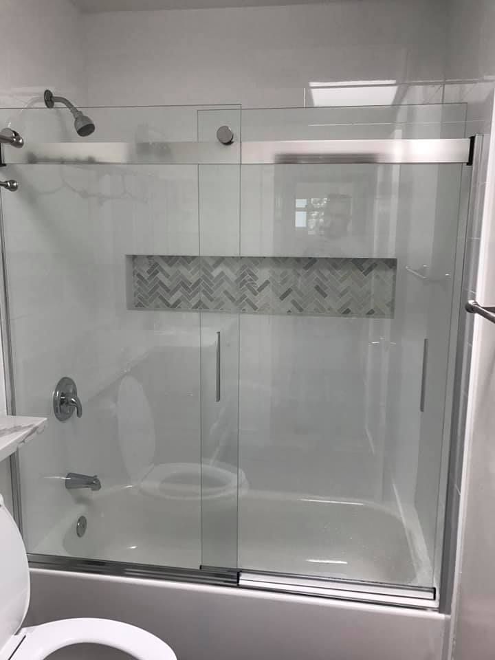 Bathroom with white bathtub and sliding glass shower doors, with grey tile accent.