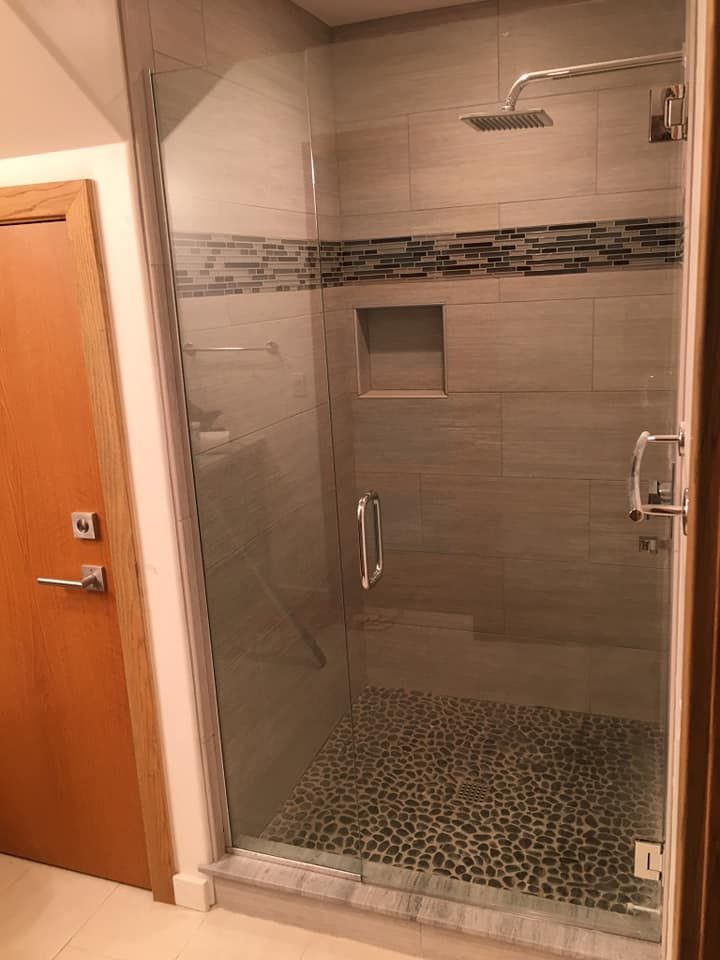 Modern shower with glass door, stone floor, and gray tile walls; recessed shelf.