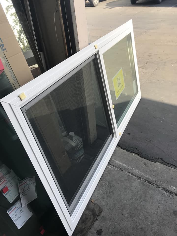 White sliding window with screen and glass, resting on concrete.