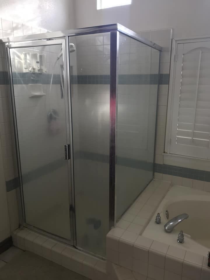 Shower enclosure next to a bathtub; glass doors with frosted glass, silver trim and a blue band.