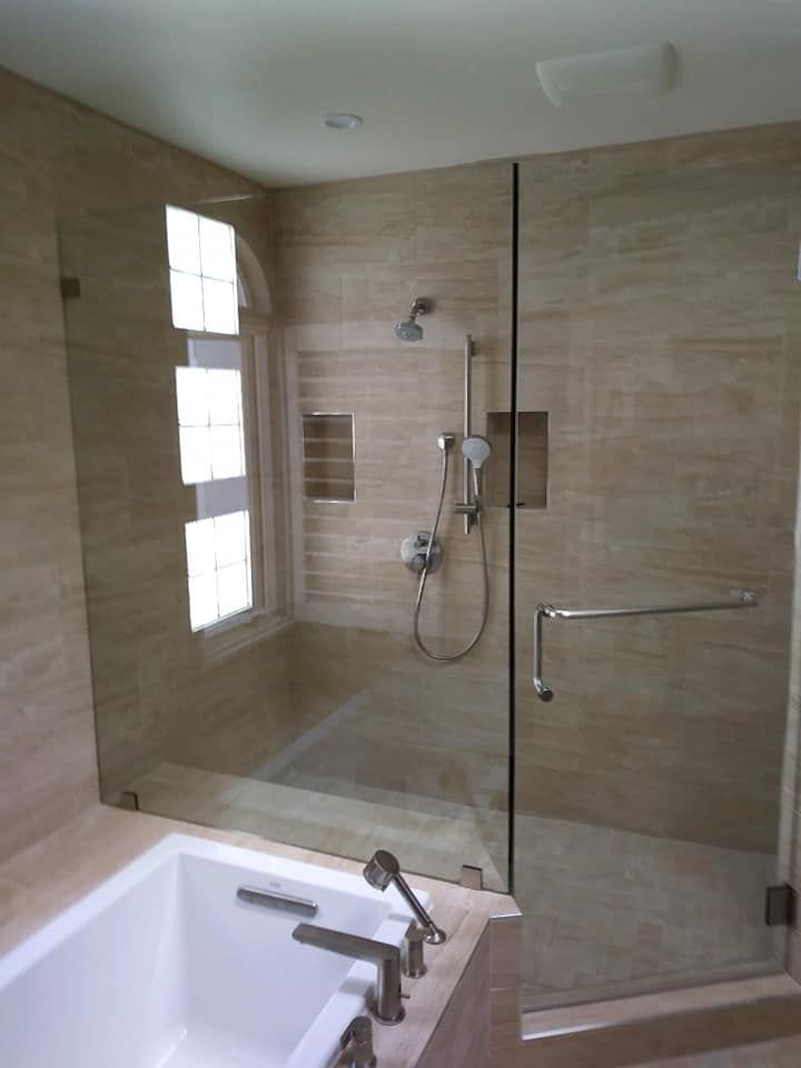 A walk-in shower with beige tile walls, glass doors, and a built-in bench, next to a bathtub.