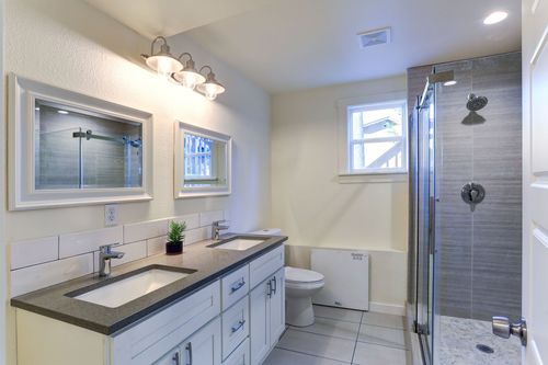 Bright modern bathroom with vanity, mirrors, toilet, window, and glass shower enclosure