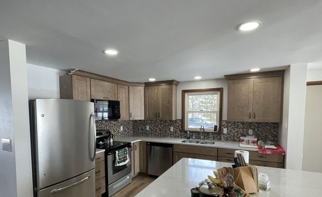 Modern kitchen with stainless steel appliances, light wood cabinets, tile backsplash, and a white island countertop