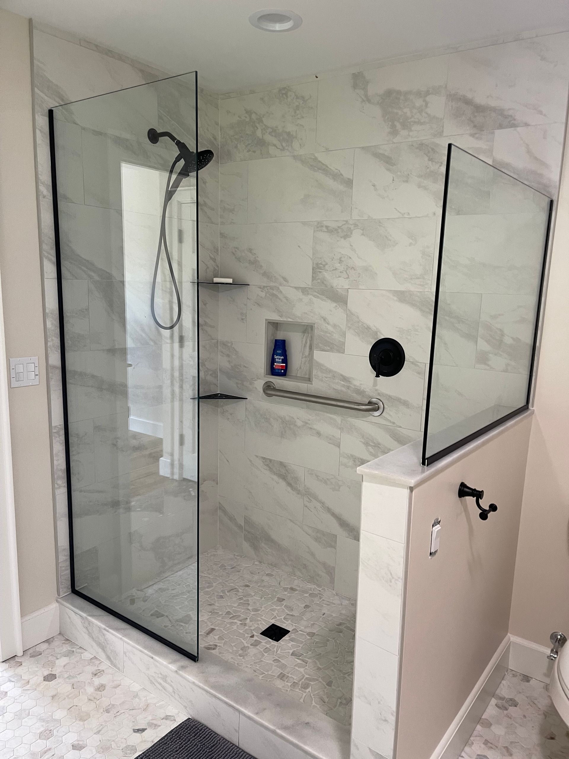 Modern marble-tiled shower with glass panels, black fixtures, and built-in shelf in a bathroom.