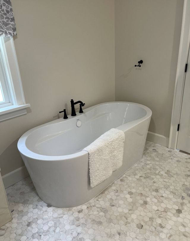 Modern bathroom with a freestanding white tub, black faucet, and light mosaic tile floor.
