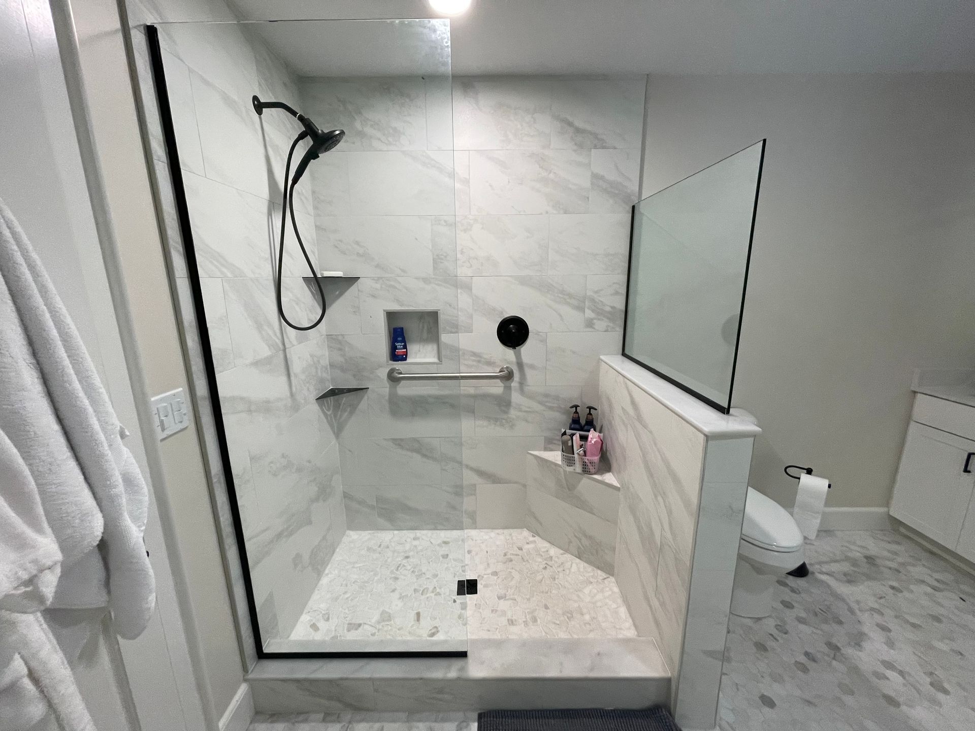 Modern bathroom with a glass-enclosed walk-in shower, white marble tile, and a wall mirror