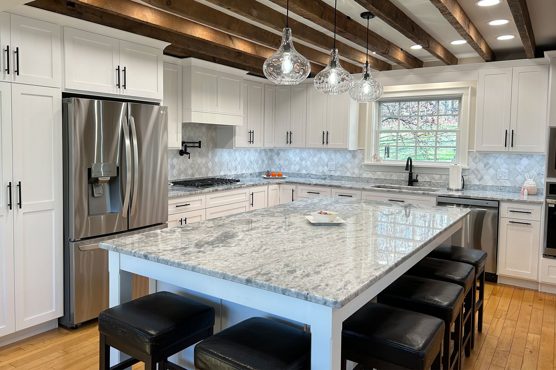 Bright modern kitchen with white cabinets, granite island, stainless fridge, and wood beams