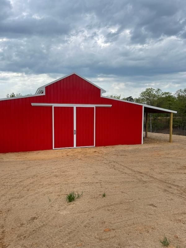 Front view of a custom red metal barn with sleek white trim and extended coverage.