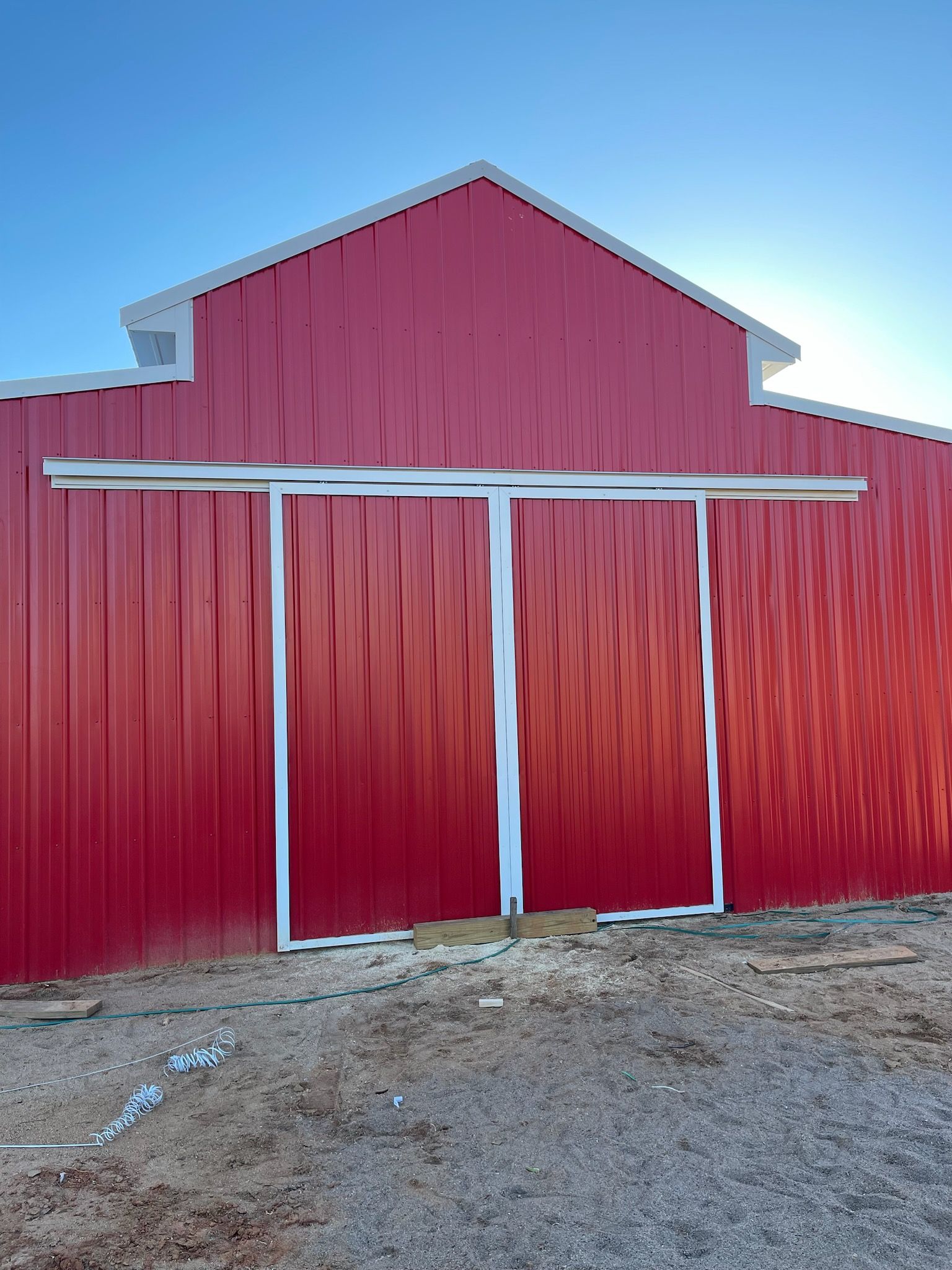 Custom red barn with white-trimmed doors nearing completion.