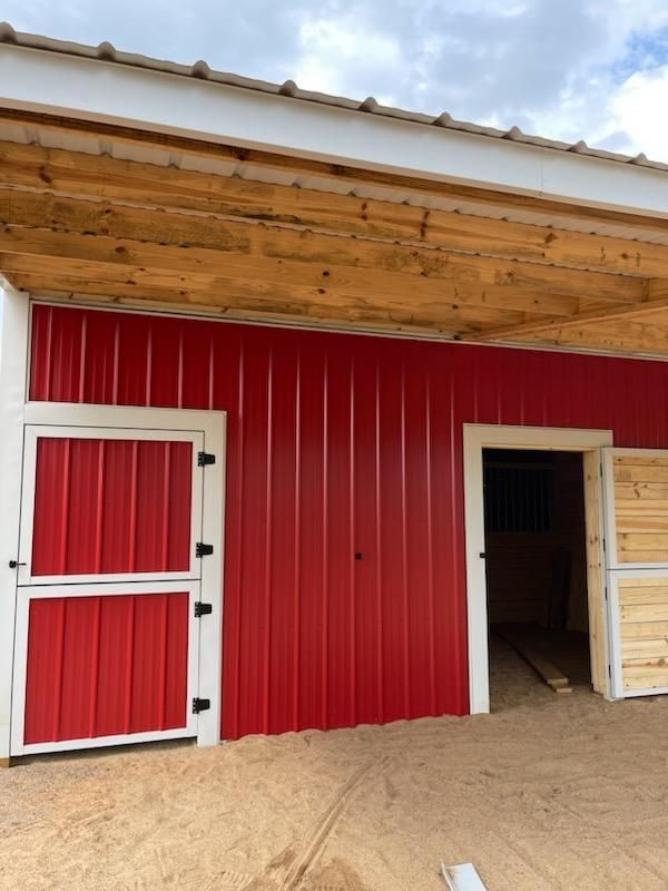 Custom red barn with white-trimmed doors nearing completion.