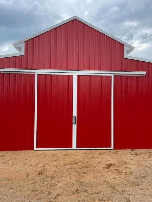 Red metal barn with symmetrical white-trimmed sliding doors under a cloudy sky.