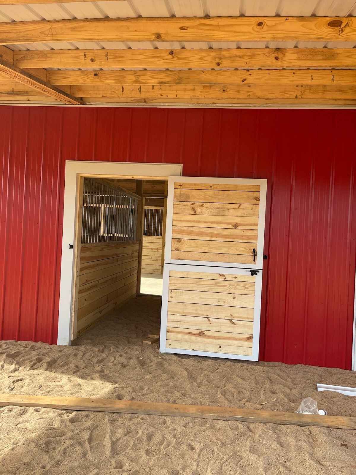 Open wooden Dutch door leading into a red metal barn with wood interior and stall partitions.