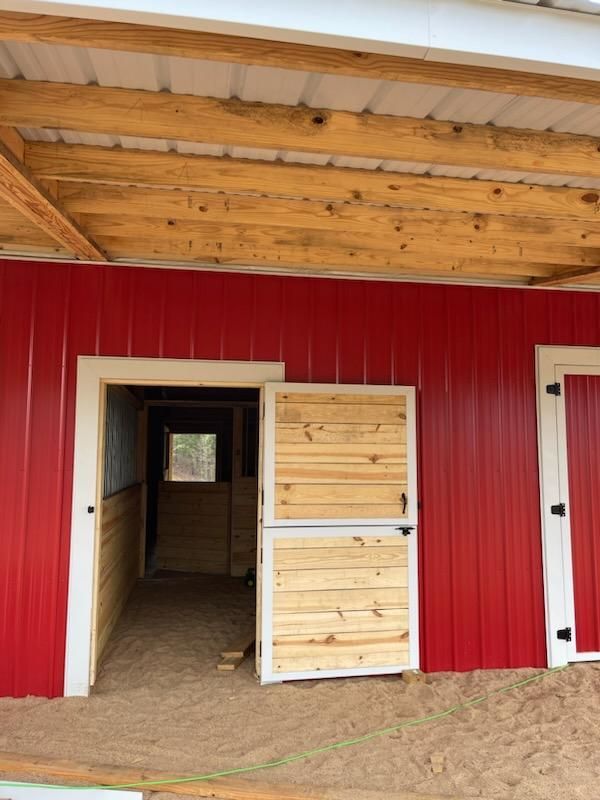 Two red Dutch doors with white trim and black hinges on a red metal barn under a wooden overhang.