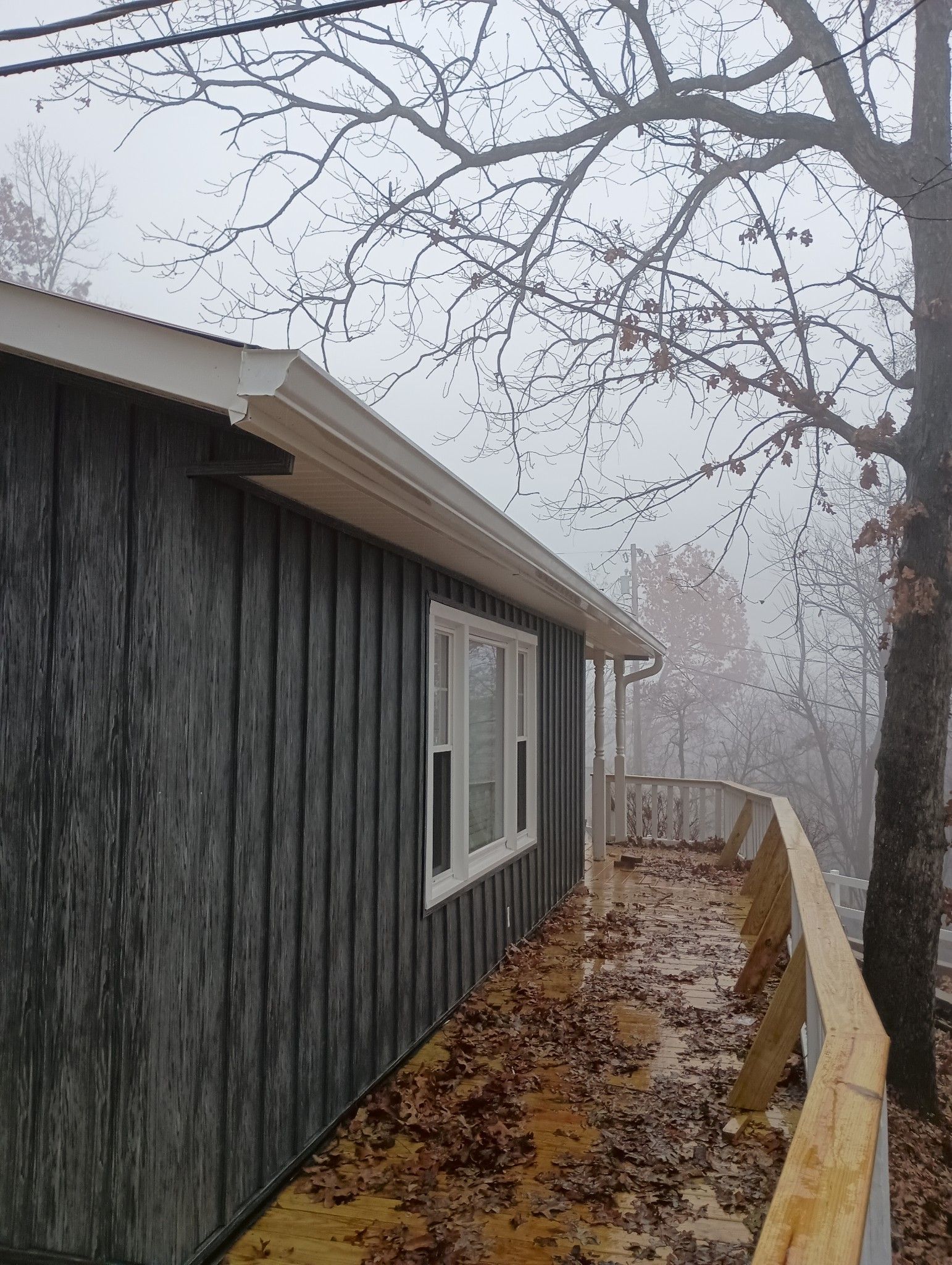 A house with a fence and a tree in the background on a foggy day.