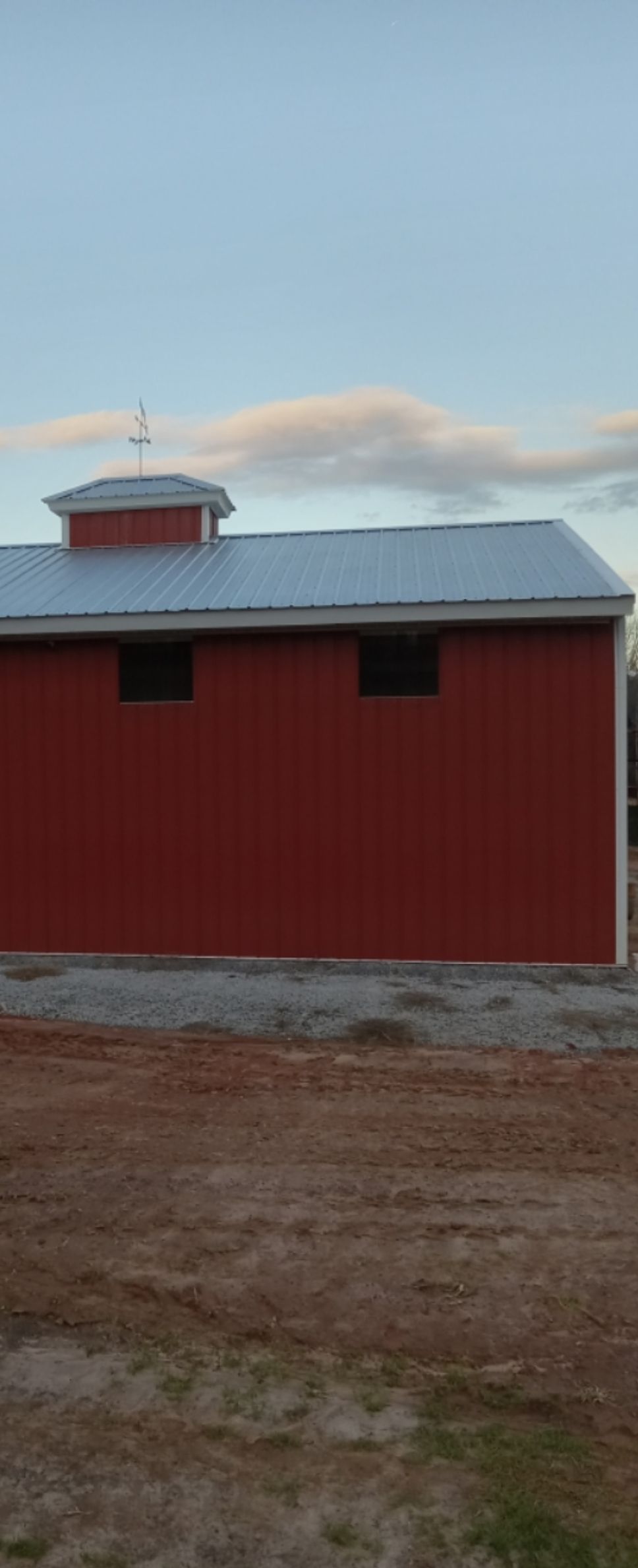 A red barn with a white roof is sitting in the middle of a dirt field.