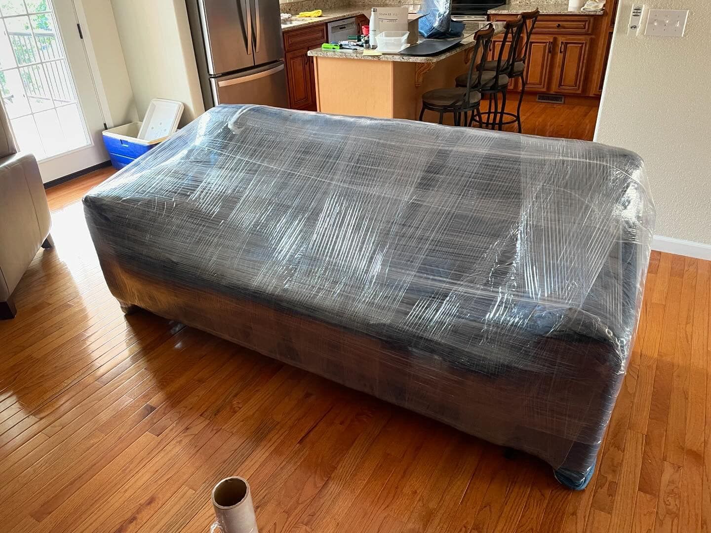 A couch is wrapped in plastic wrap in a living room.
