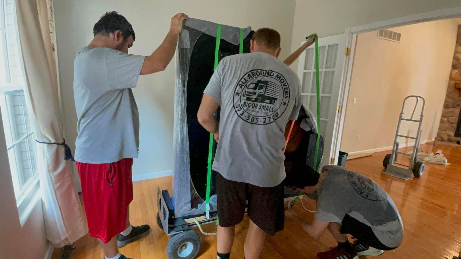 A group of men are moving a piano in a living room.