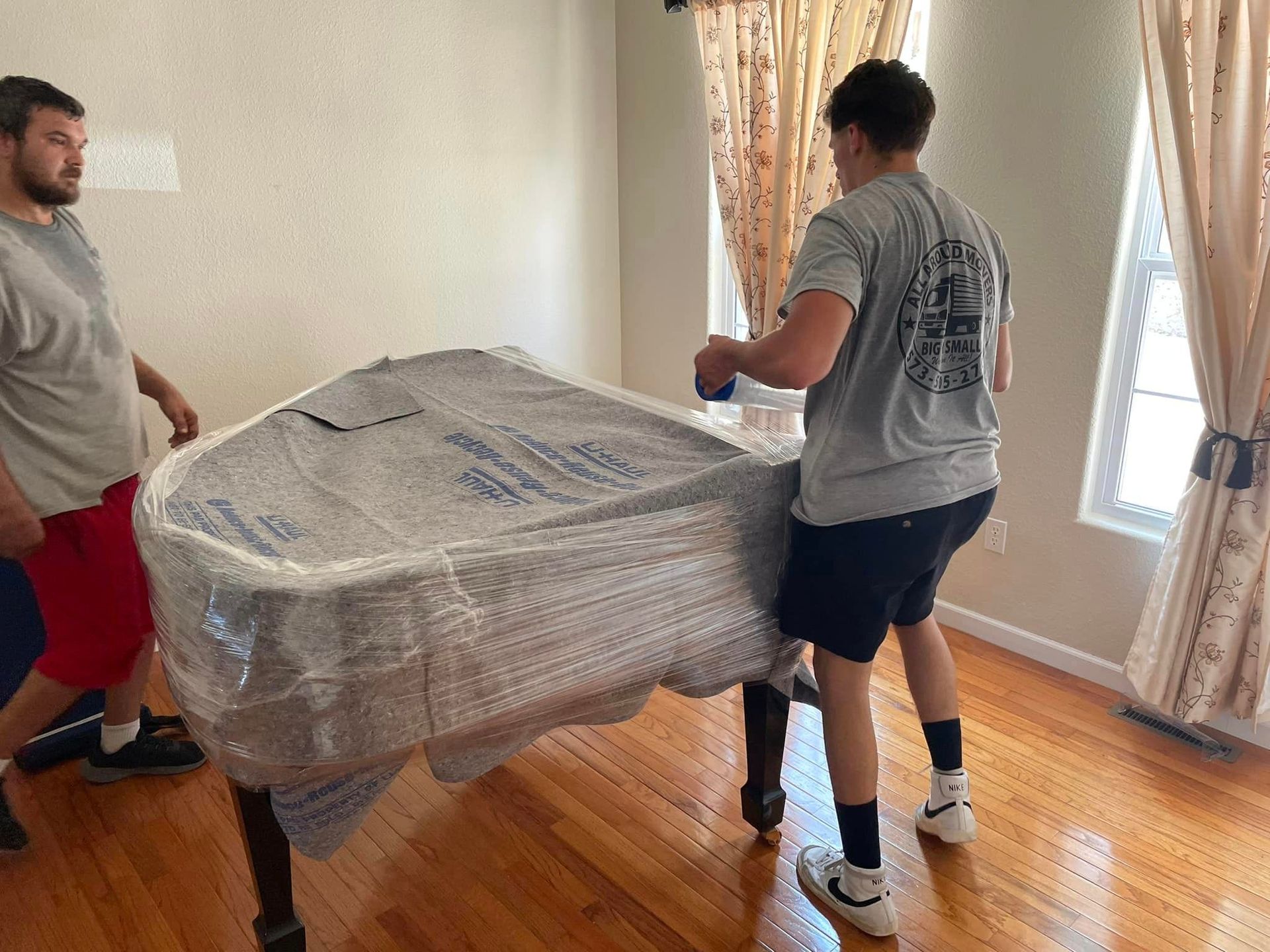 Two men are moving a piano in a living room.