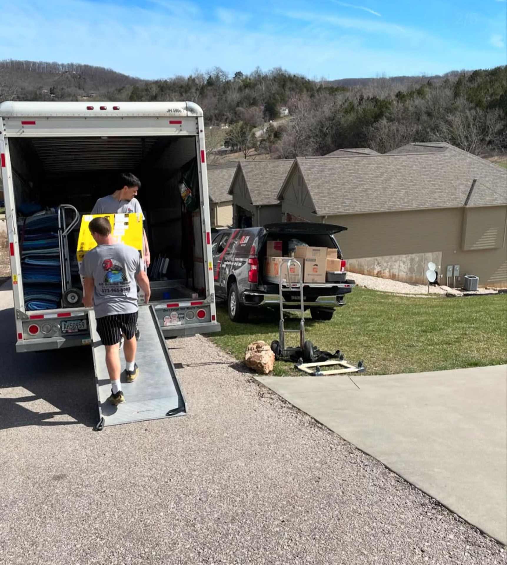 Two men are loading a truck with a ramp in front of a house