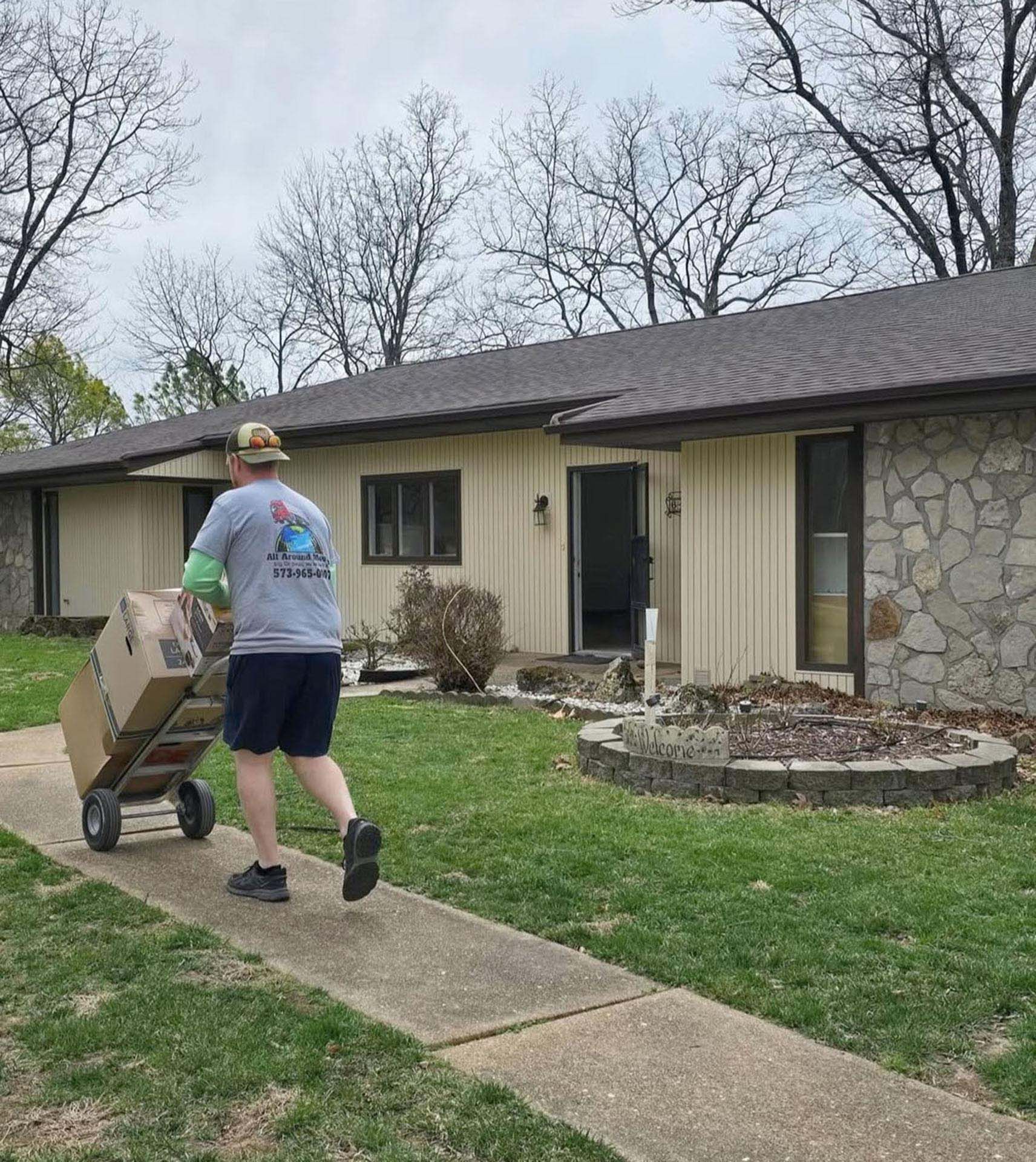 A man is moving cardboard boxes down a sidewalk in front of a house