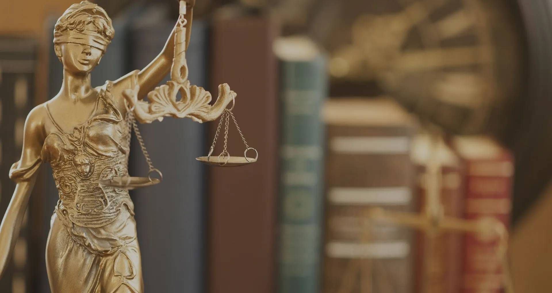 A statue of justice holding a scale in front of a row of books.