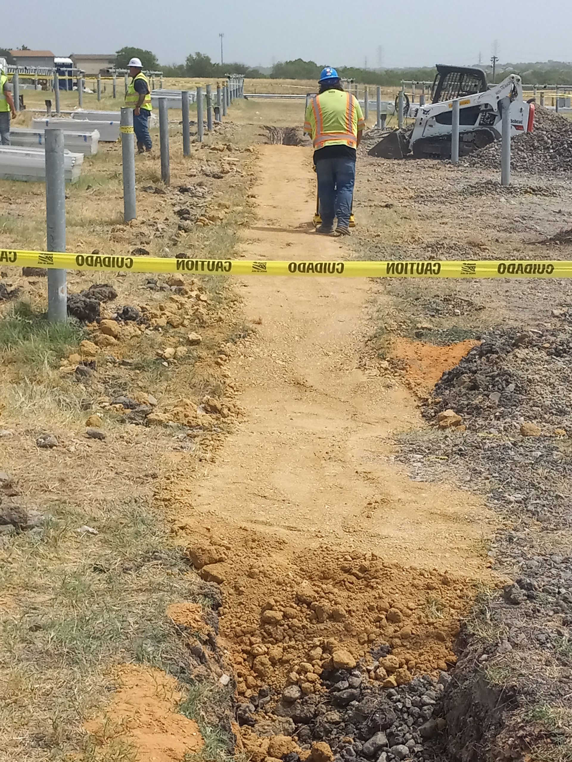 Construction worker walking on a cleared path at a solar panel installation site, marked with caution tape.