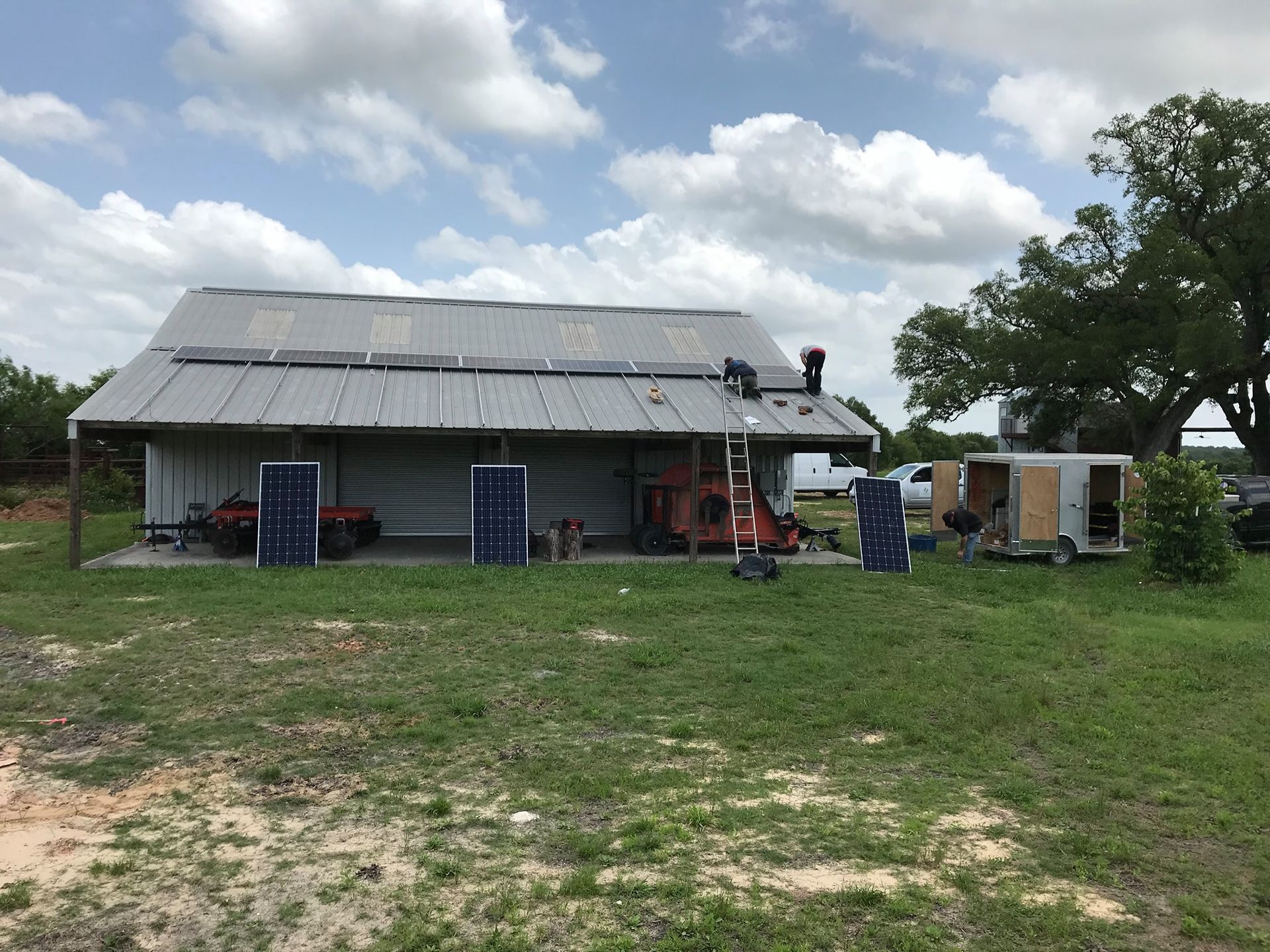 A barn with solar panels on the roof is sitting in the middle of a grassy field.