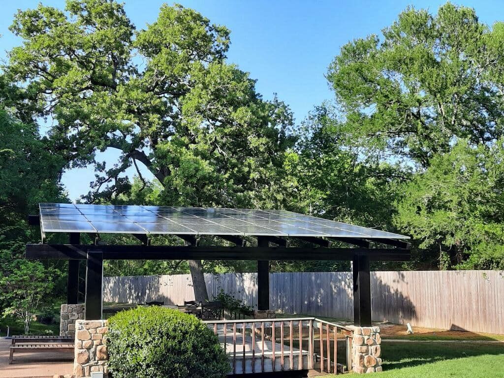 A gazebo with a solar panel on top of it in a backyard surrounded by trees.