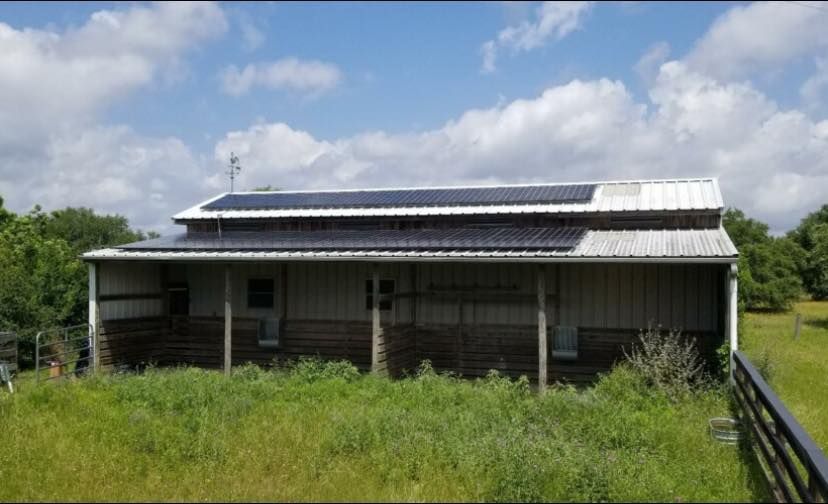 A house with solar panels on the roof is sitting in the middle of a grassy field.
