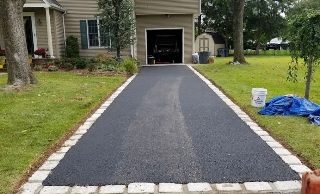 Freshly paved asphalt driveway with brick border leading to a garage door.