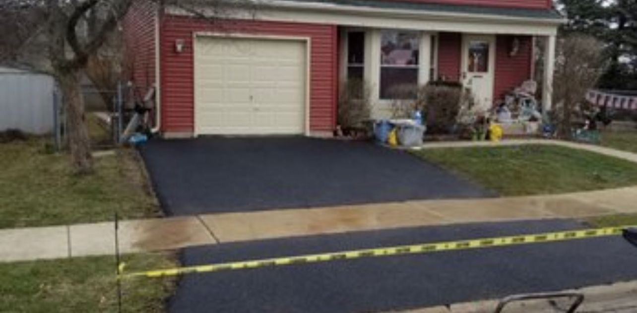 A house with a freshly paved driveway, yellow caution tape in the foreground.