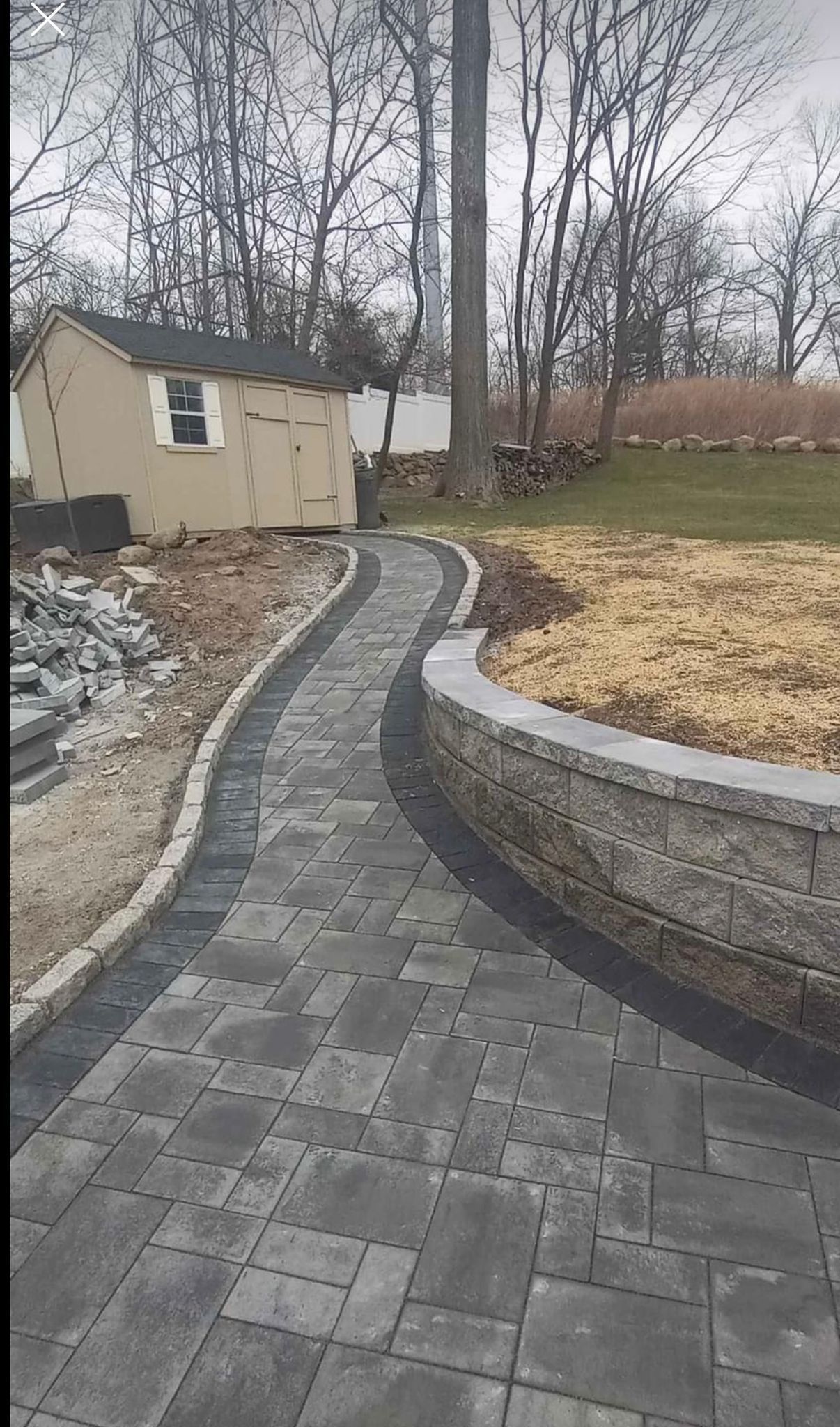 Stone paver walkway next to retaining wall and shed in backyard.