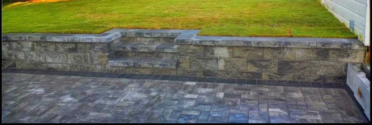 Stone wall separating a grassy area from a brick patio.