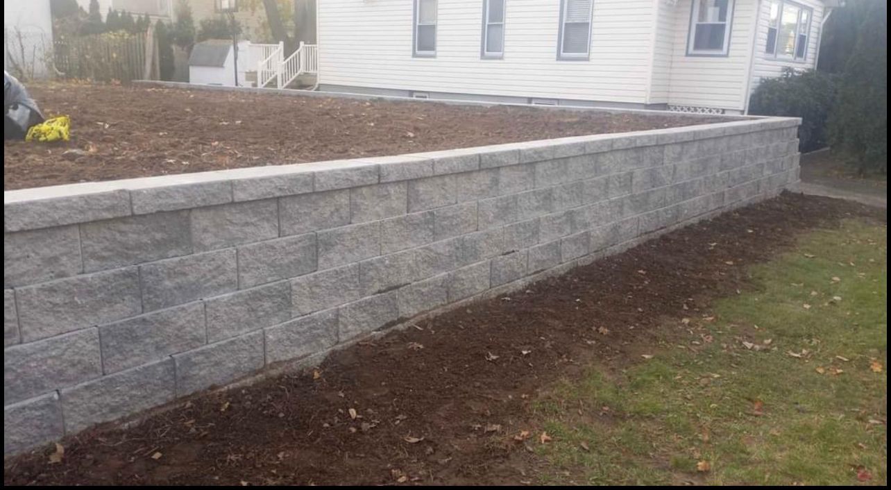 Gray block retaining wall in front of a house, with a freshly mulched area and grass in the foreground.