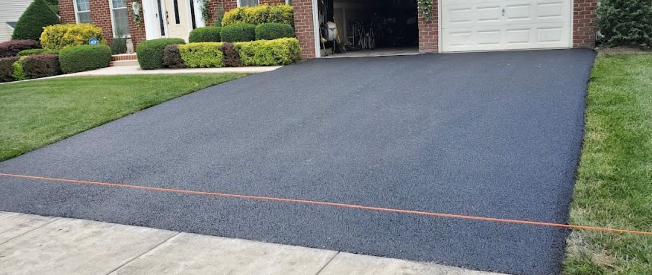 Newly paved asphalt driveway with green grass and house in the background.
