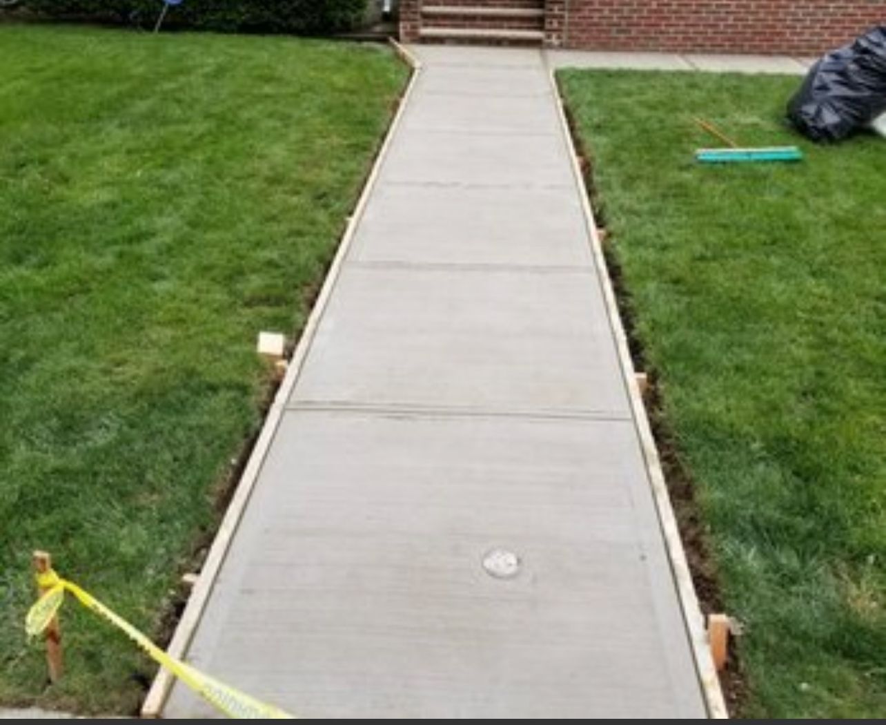 Freshly poured concrete sidewalk flanked by green grass. Wooden forms border the walkway.