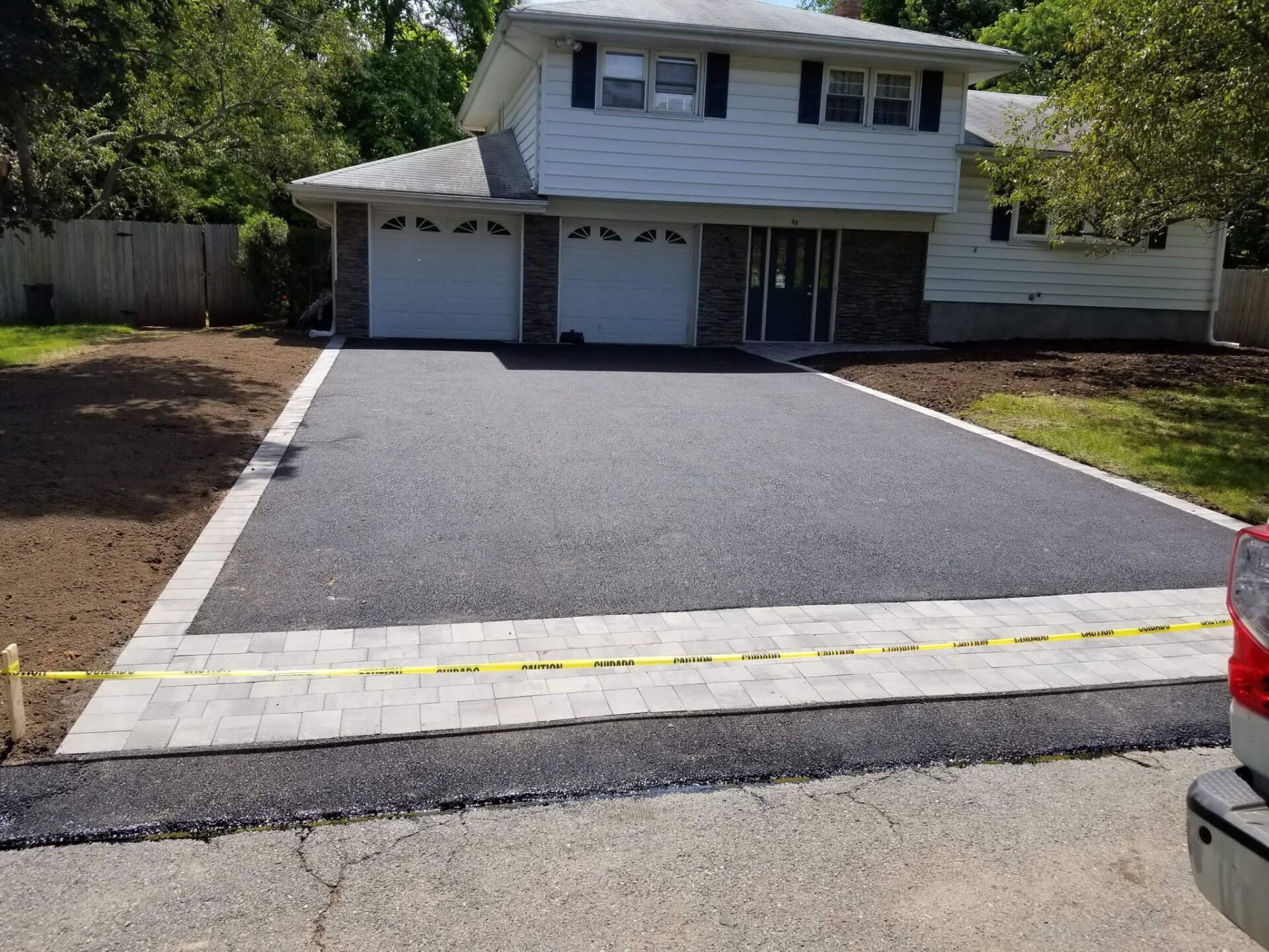 Newly paved asphalt driveway with a stone border in front of a two-story house.