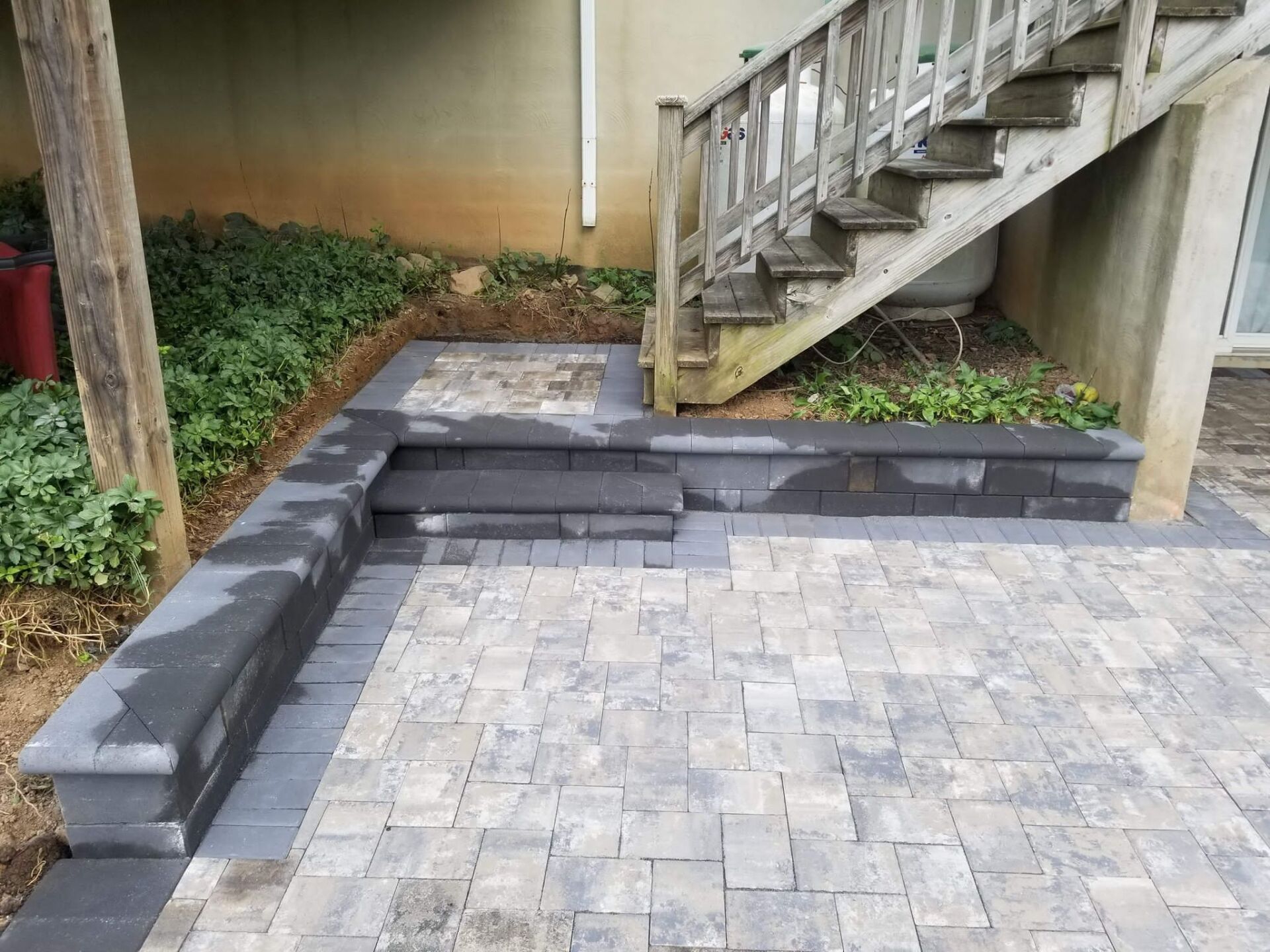 Paver patio with steps and retaining wall leading to wooden stairs.