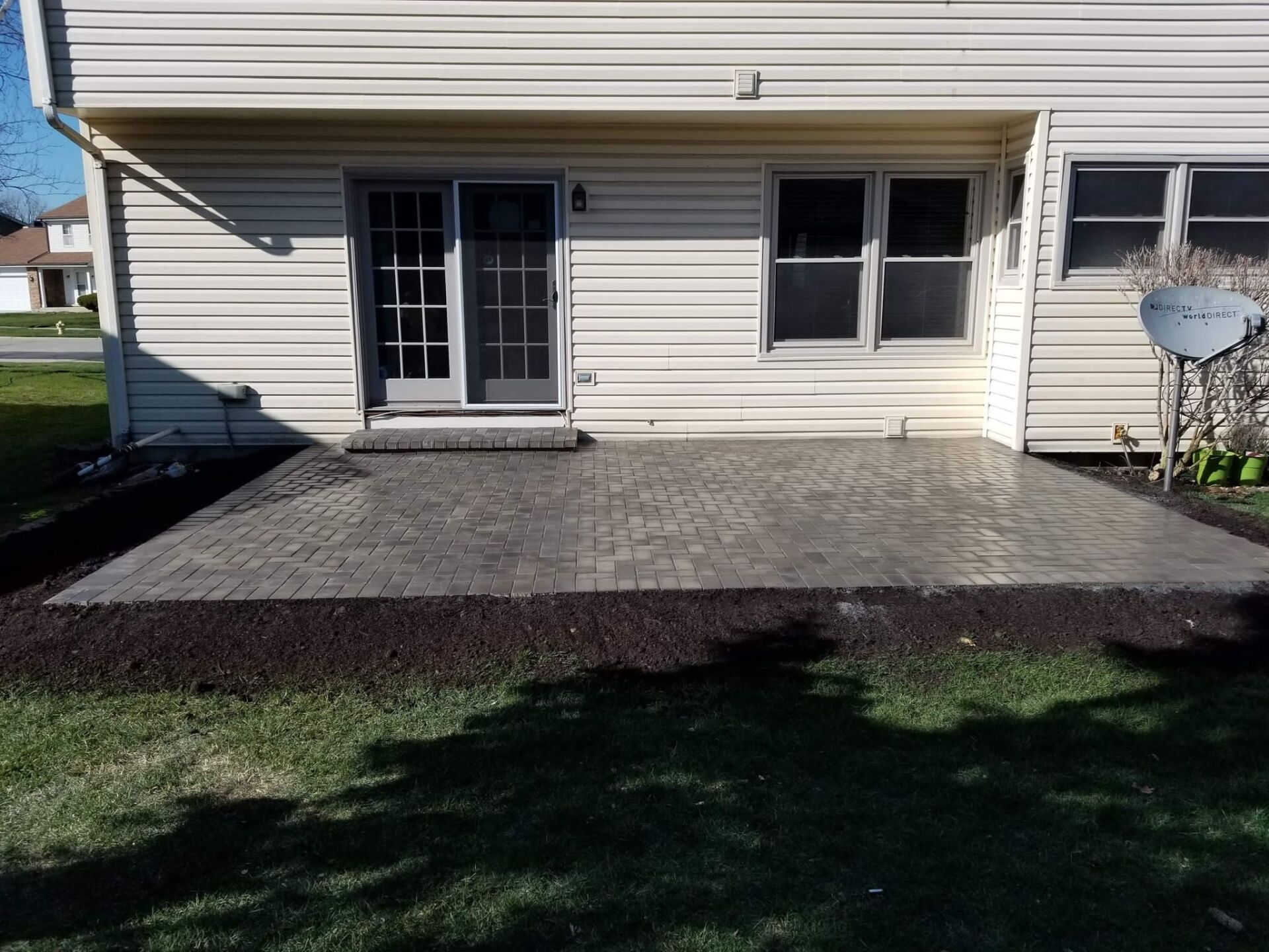 Backyard patio with pavers and sliding glass door. Mulch borders patio; siding is beige.