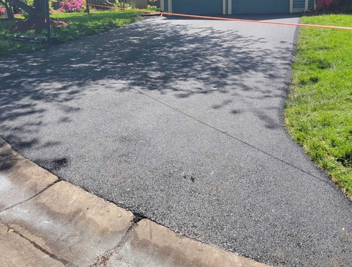 Asphalt driveway curving from street to a blue-green garage, bordered by grass and a concrete curb.