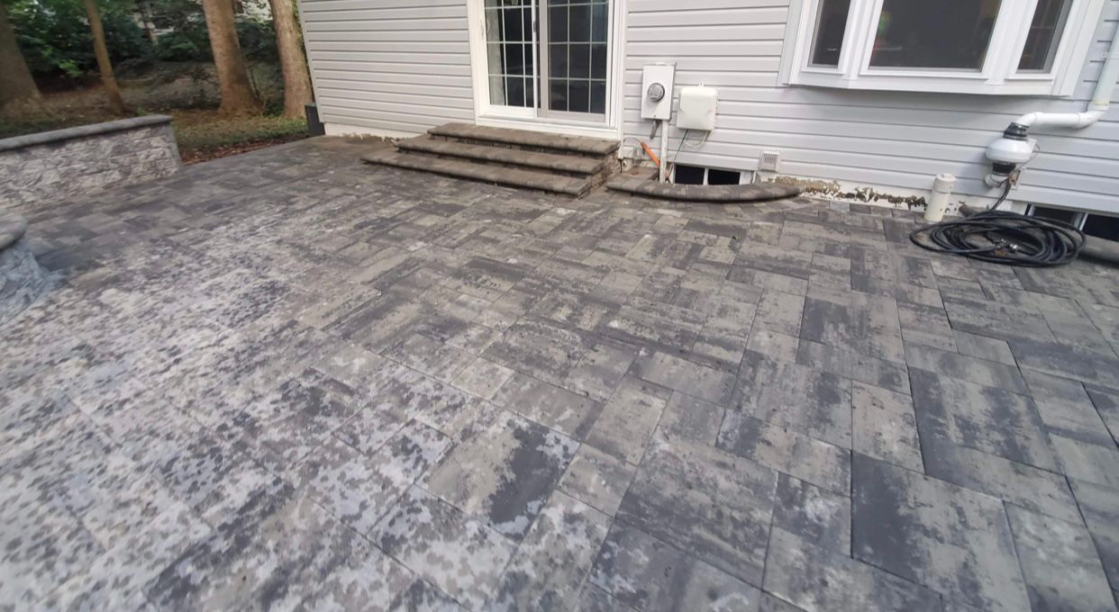 Brick patio in varying shades of gray leading to a house with steps and a white door.