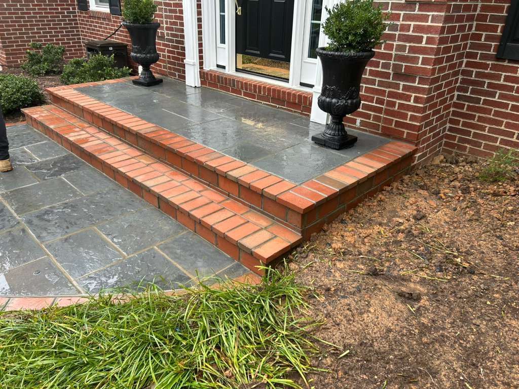Brick steps leading up to a house entrance with stone patio and potted plants.