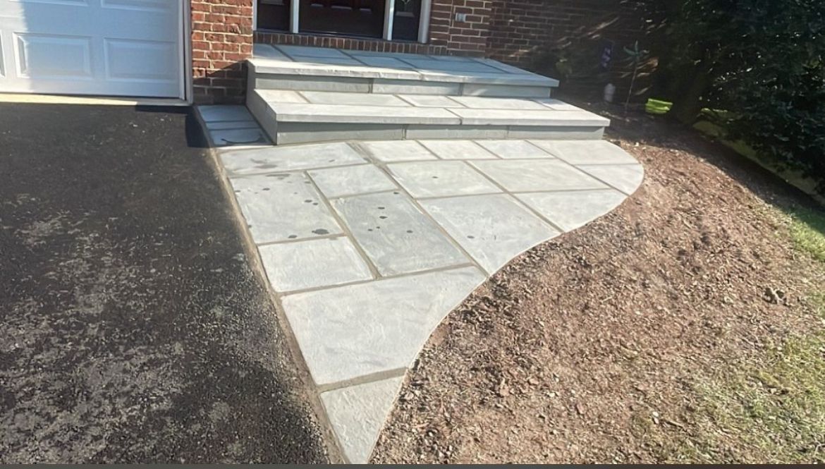 Stone walkway leading to house steps, with a lawn on the right and driveway on the left.