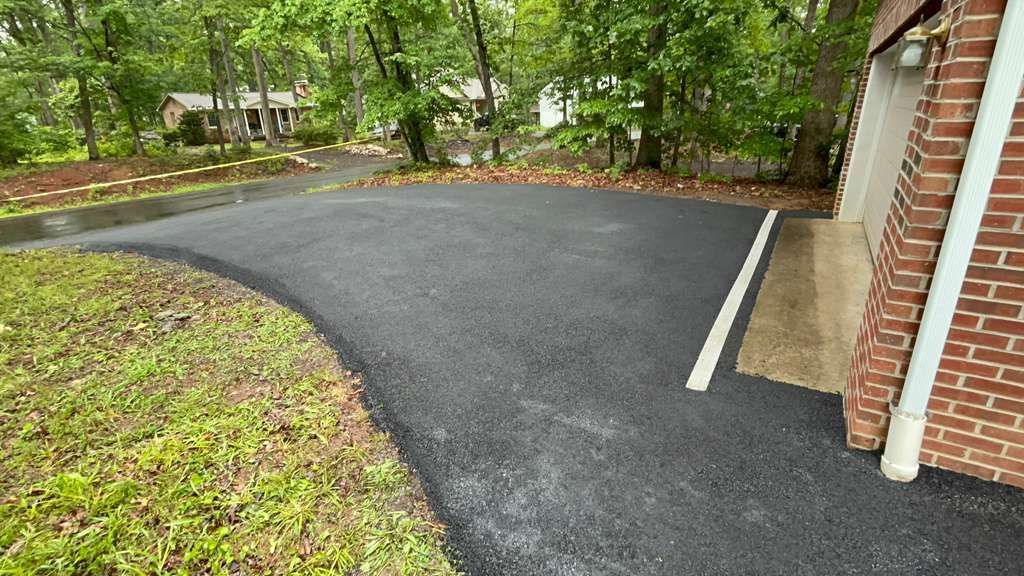 Freshly paved black asphalt driveway curves towards a brick building with a white downspout.