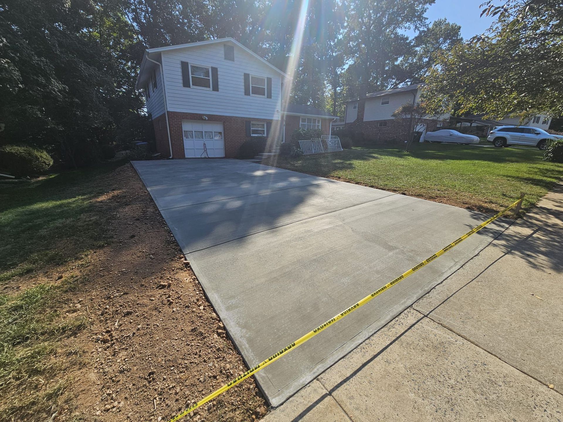 Newly poured concrete driveway in front of a two-story house with a garage. Yellow caution tape is present.