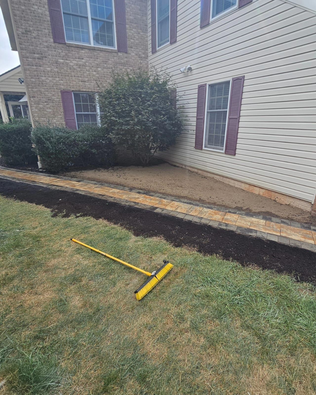 A house exterior with newly mulched flower bed and a yellow landscape rake on the grass.