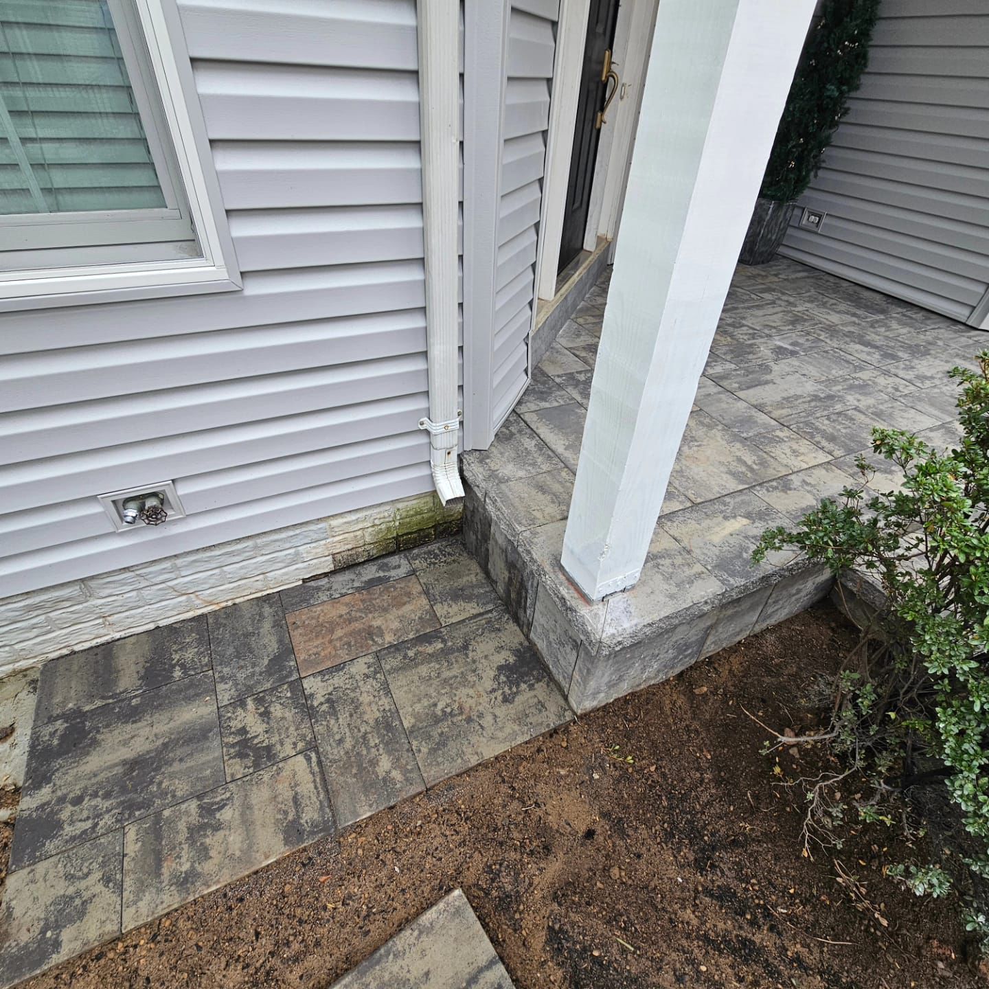 Gray house exterior with stone walkway and porch steps. Downspout, pillar, and greenery.