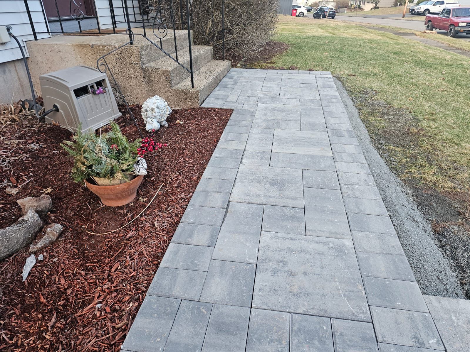 Gray paver walkway leading to house steps. Mulched flowerbed with potted plant beside the path.