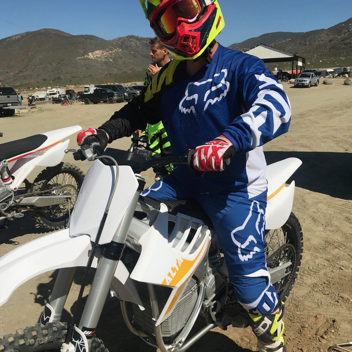 A man wearing a blue and white fox outfit is riding a dirt bike