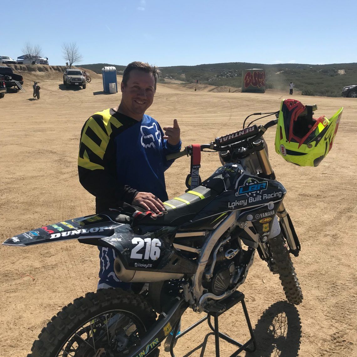 A man is standing next to a dirt bike with the number 216 on it